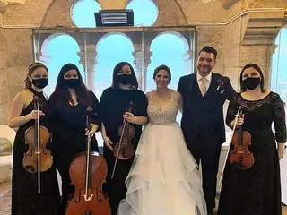 A vonósnégyes maszkban, fekete ruhában az ifjú párral a Halászbástya ívei előtt