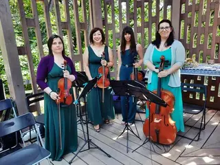 A vonósnégyes zöld és türkiz ruhában, hangszerekkel egy fa pavilonban
