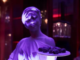 Fehérre festett élőszobor-artista lila fényben, édességes tálcával